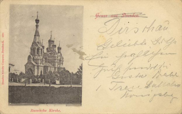 Eine schwarz-weiße Postkarte mit der Kirche des Erlöserbluts in Dresden, Deutschland, umgeben von Bäumen unter einem klaren blauen Himmel, mit deutschem Text auf der rechten Seite.