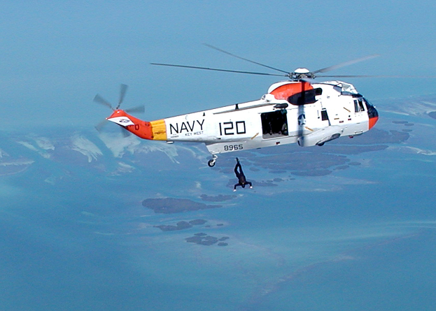 Ein Rettungshubschrauber fliegt über einen See mit einer Person in der Luft, vor dem Hintergrund des Himmels.