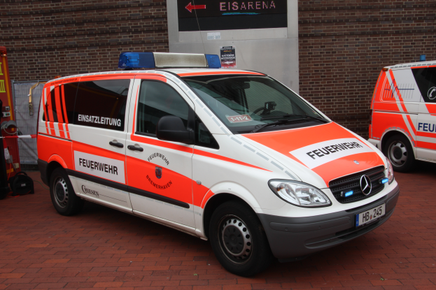 Zwei Rettungswagen nebeneinander vor einem Gebäude mit einer Wand im Hintergrund geparkt, ein Feuerlöscher und andere Gegenstände auf der linken Seite sichtbar.
