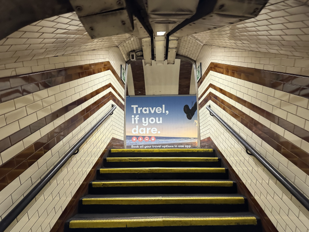 Eine Treppe in einer U-Bahn-Station mit einem 'Reise, wenn du wagst'-Schild oben, flankiert von Geländern und StationWsänden im Hintergrund.