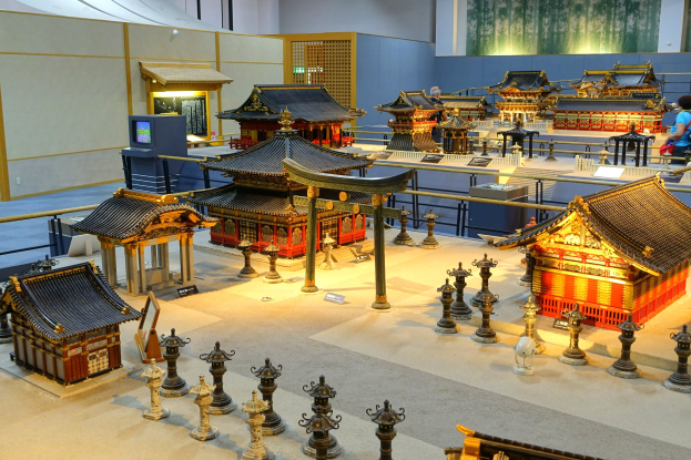 Ein großer Raum im Tokyo Toy Museum mit Miniaturgebäuden, Pfählen, Geländern, Texttafeln, einem Bildschirm und verschiedenen anderen Gegenständen, die von Menschen betrachtet werden.