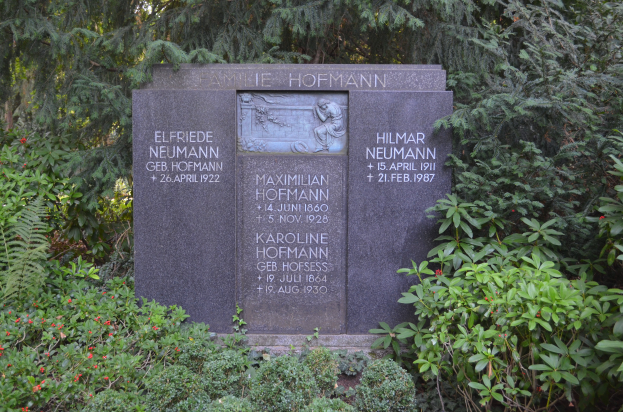 Ein Gedenkstein in einem Park umgeben von B"{a}umen und Pflanzen mit eingravierter Inschrift, wahrscheinlich zur Erinnerung an Holocaust-Opfer.