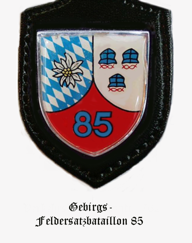 Ein rundes Abzeichen mit der Zahl 85 in der Mitte, umgeben von einem Lorbeerkranz, und deutschem Text unten.