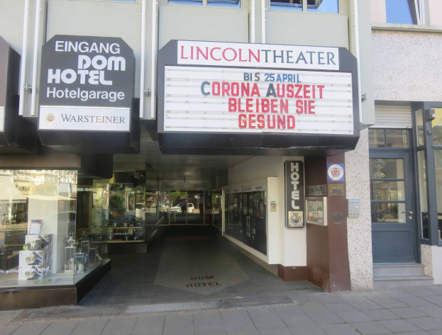 Außenansicht des Lincoln Theaters in Berlin, Deutschland, mit Glasfenstern und -türen sowie einer Schautafel und einem Blick ins Innere, der auf eine belebte städtische Umgebung hinweist.
