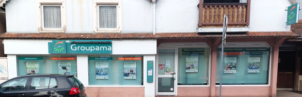 Schwarzes Auto vor einem Gebäude mit einer "Assurances et Banque Groupama"-Schilder parkend, Fenstern, einer Straßenlaterne, Papieren auf der Scheibe und einem bewölkten Himmel.