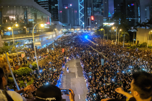 Eine große Menschenmenge steht nachts auf einer Straße, beleuchtet von Straßenlaternen, wobei einige Mobiltelefone halten, während einer gewalttätig gewordenen Hongkonger Protestaktion.