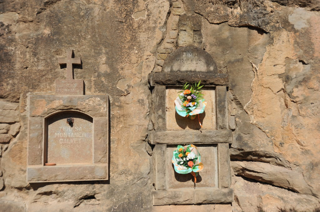 Denkmale in eine Wand gemeisselt mit Blumensträußen davor.