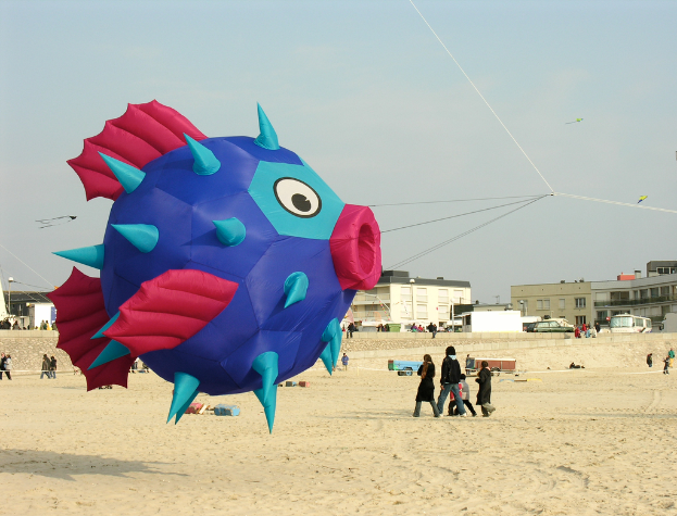 Ein fischförmiger Luftballon umgeben von Menschen, Autos und Gebäuden.