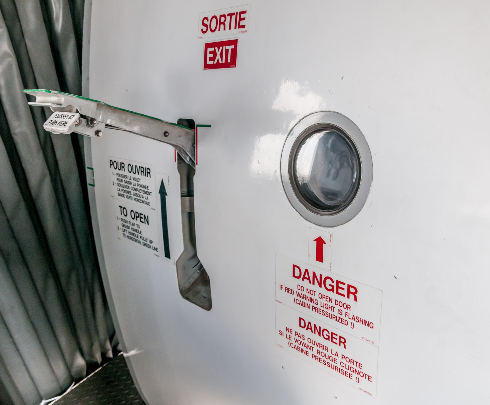 Nahaufnahme eines Metallbehälters mit Türgriff, einer "Gefahr"-Aufschrift und einem Vorhang auf der linken Seite.