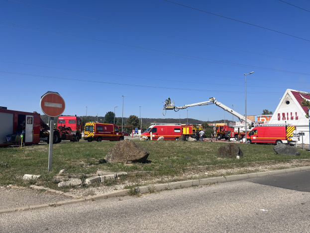 Feuerwehrl├Ąrme auf der Stra├če neben einem Haus geparkt, mit B├Ąumen und bew├Âlktem Himmel, wahrscheinlich nach einem Tankstellenbrand.