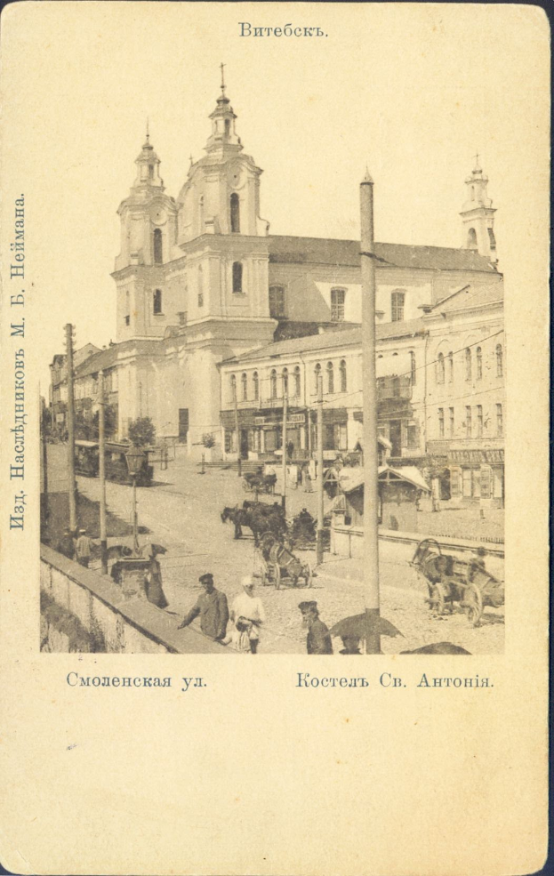 Ein altes Foto einer belebten Stadtstraße mit einer Kirche im Hintergrund, das Gebäude, Pfähle, Menschen, Karren, Pferdefuhrwerke und Bäume an der Straße zeigt, mit Text am unteren Bildrand.