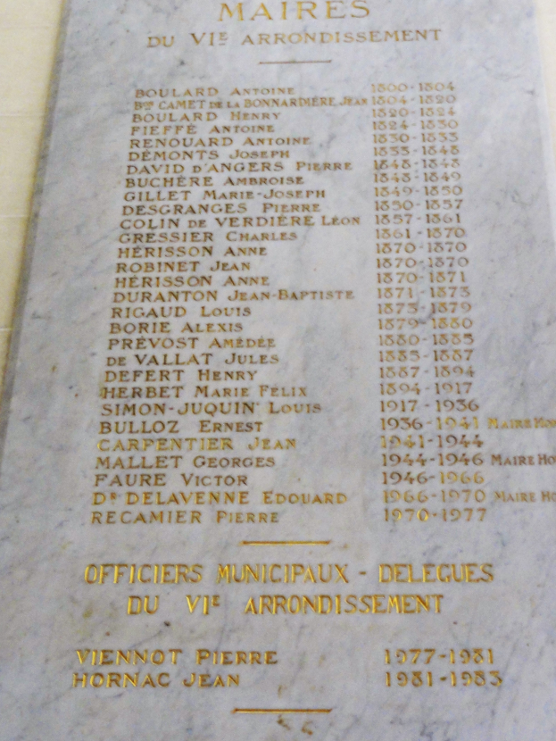 Ein steinernes Schild an einem Gebäude mit der Aufschrift "Maires du Vie Arrondissement" in fetter Schrift, umgeben von einem dekorativen Rahmen.