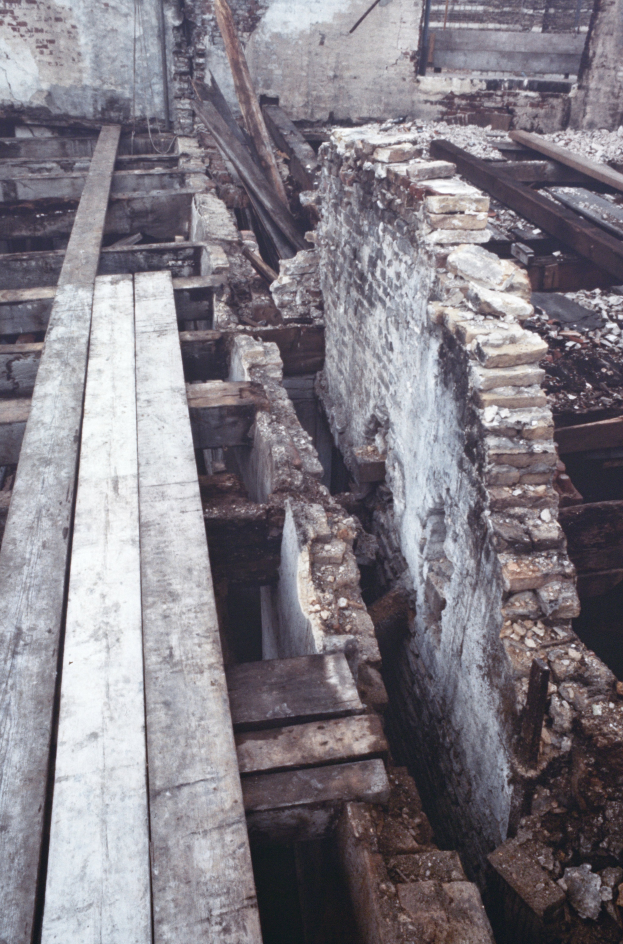 Ein altes Gebäude mit Schutt aus Holzplanken und Steinen auf dem Boden, mit einer Wand im Hintergrund, die den Abriss vermuten lässt.