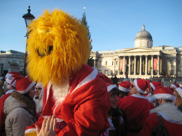 Mann in Santa-Kostüm mit Tiger-Maske steht mit anderen in Santa-Kostümen vor einem Gebäude