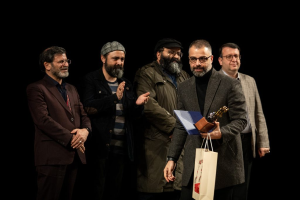 Eine Gruppe von Männern auf einer Bühne bei Nacht, einer hölt eine Tasche und eine Trophäe, feiernd die Eröffnung des Berliner Filmfestivals.