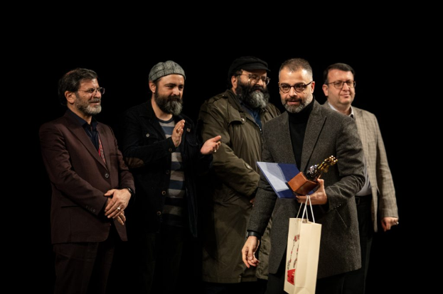 Eine Gruppe von Männern auf einer Bühne bei Nacht, einer hölt eine Tasche und eine Trophäe, feiernd die Eröffnung des Berliner Filmfestivals.