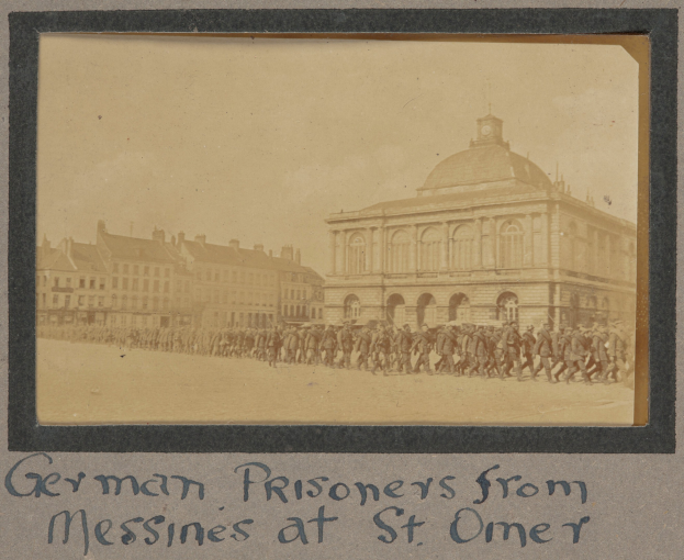 Deutsche Kriegsgefangene aus Messines vor einem Gebäude mit einem klaren blauen Himmel im Hintergrund, Text unten.