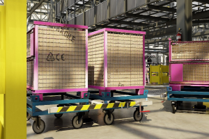 Großer Lagerraum mit zahlreichen Kisten auf Wagen, eine gelbe Säule links, ein Feuerlöscher rechts, Metallstangen im Hintergrund und sichtbarer Boden.