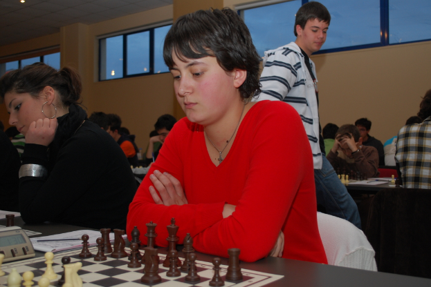 Eine Gruppe von Menschen spielt Schach, wobei eine Person in der Mitte ein rotes Kleid trägt.