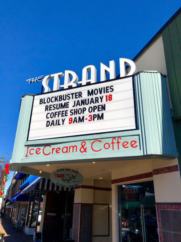 Der Strand-Blockbuster-Kino startet am 18. Januar Kaffeehaus mit einem Namen Brett, einem Straßenschild, einer Gruppe von Bäumen, einigen Topfpflanzen und einem bewölkten Himmel.