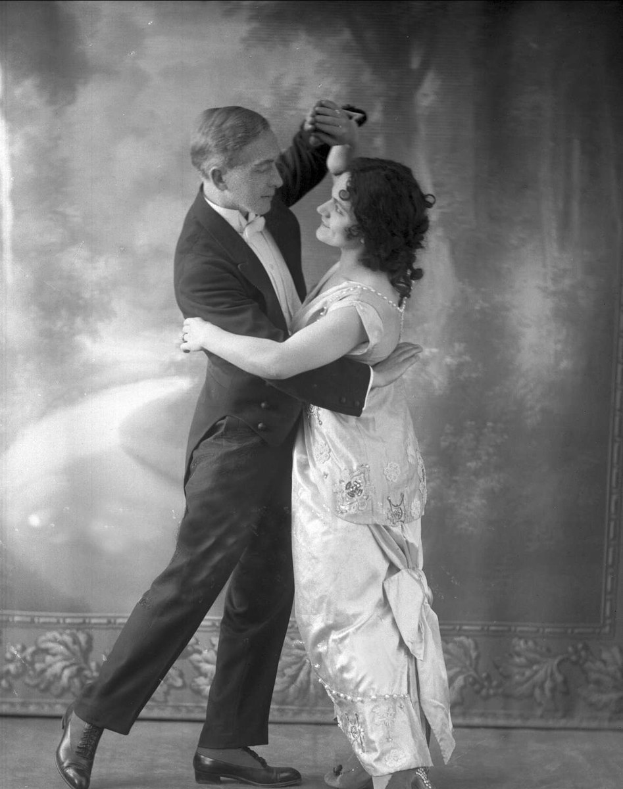 Schwarz-weiß-Foto eines Mannes in einem Anzug und einer Frau, die Tango tanzen, mit aufwändigen Wanddesigns im Hintergrund.