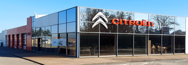 Außenansicht eines Citroën-Händlergeschäfts mit Glaswänden und -türen, einer Straße davor und einem klaren blauen Himmel.