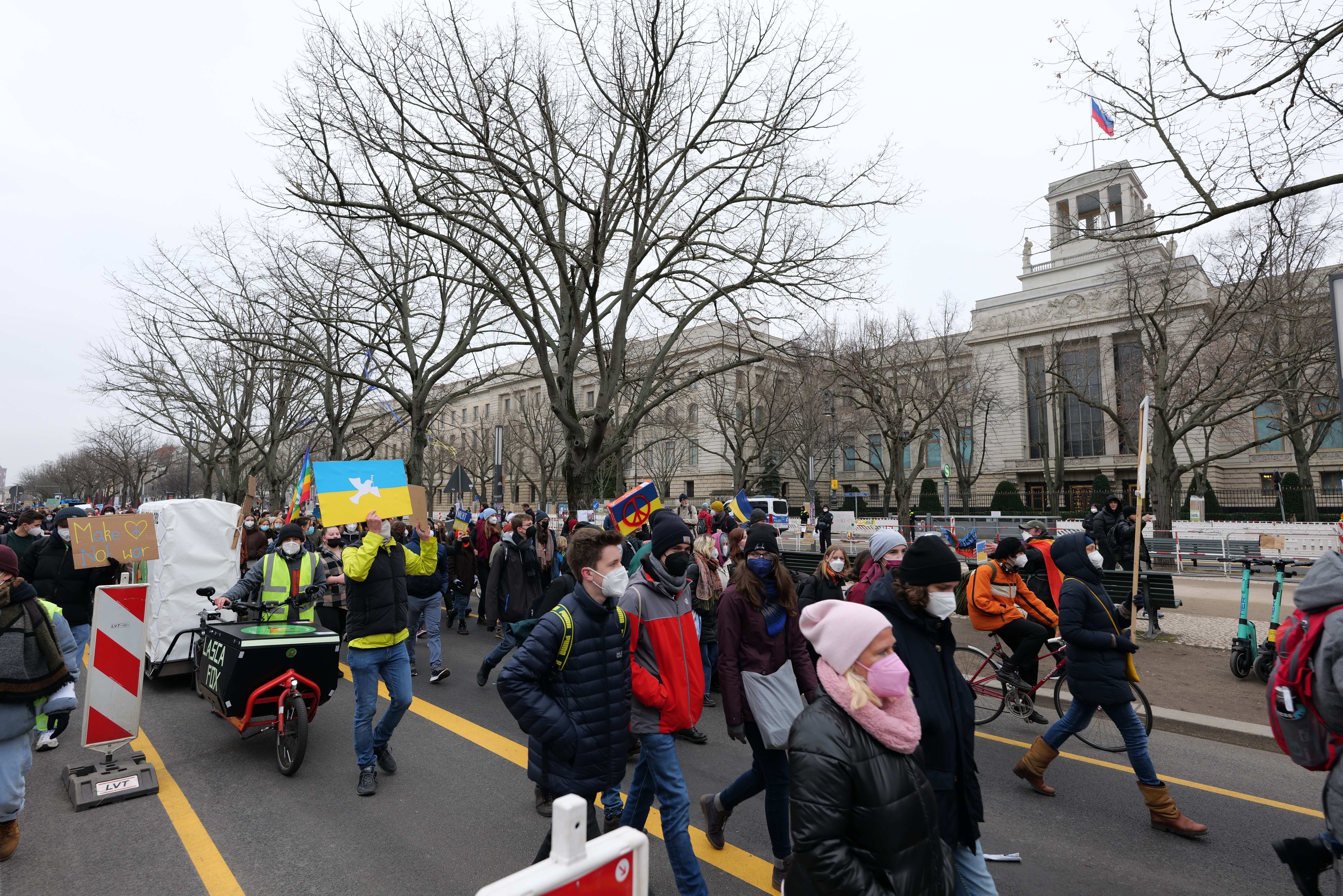 Eine große Gruppe von Menschen marschiert bei einer Protestaktion durch eine Straße in Washington, D.C., mit Schildern und Transparenten, während einige Fahrräder fahren, unter einem klaren blauen Himmel.