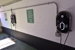 Ein Elektrofahrzeug-Ladestation in einer Tiefgarage mit zwei Ladepunkten an der Wand und Schildern mit Text darauf, der Boden ist unten im Bild zu sehen.