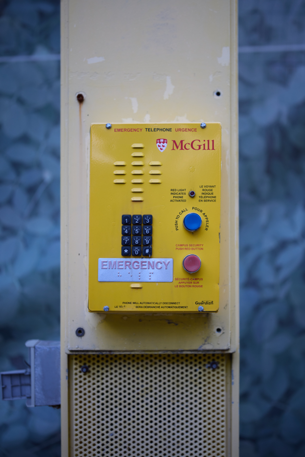 Ein gelber Notrufautomat an einer Gebäudeseite mit Knöpfen und Text für Notrufe, vor einer Wand.