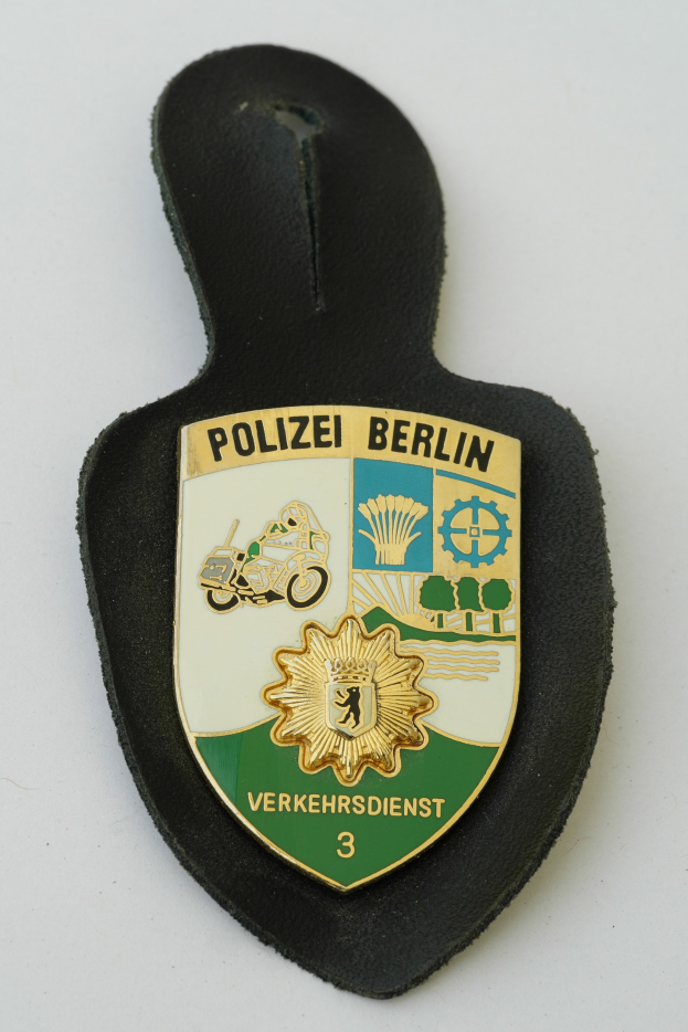 Ein schildförmiges Polizeibadge mit der Aufschrift 'Polizei Berlin' auf blauem Hintergrund, einem weißen Stern und einem weißen Rand, das auf einer Oberfläche liegt.