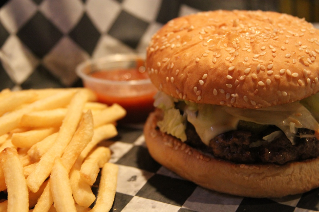 Ein Burger, eine Portion Pommes und ein kleiner Behälter mit Sauce sind auf einer Fläche zu sehen.