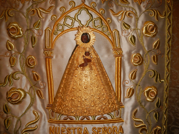 Goldbrokate Chasuble mit einer serenen Frau in einem hochgeschlossenen, langärmligen Kleid mit einem Dutt, umgeben von detaillierten Texten und Designs in einem goldenen Rahmen.