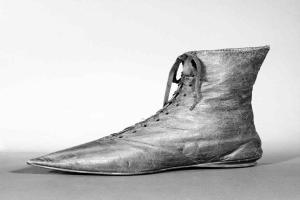 Schwarzes und weißes Foto eines Paares abgetragener, lederner Schnürstiefel mit gerundeter Spitze und niedrigem Absatz, die einen altertümlichen, zeitlosen Eindruck machen.