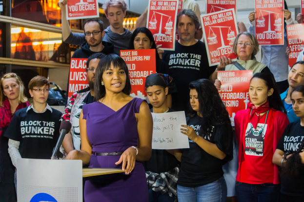 Eine Black-Lives-Matter-Aktivistin spricht in ein Mikrofon an einem Rednerpult, während sie eine Menge anspricht, die Schilder hält.