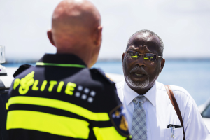 Zwei Männer im Gespräch: einer im weißen Hemd und Schlips, der andere in einer schwarzen und gelben Polizeiuniform, mit einem unscharfen Hintergrund.