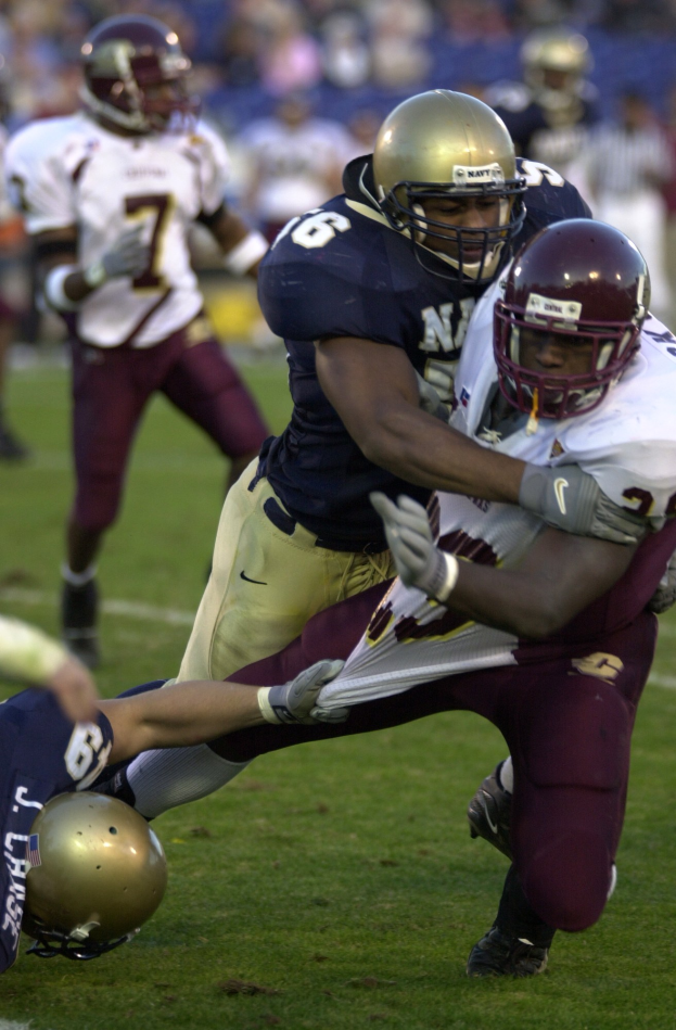 Zwei Fußballspieler in Helmen und Uniformen kollidieren auf dem Feld, während andere zusehen.