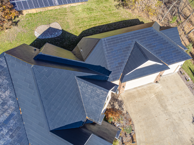 Ein Haus mit Solarmodulen auf dem Dach, umgeben von Bäumen, Gras und einem Zaun, aus der Vogelperspektive.